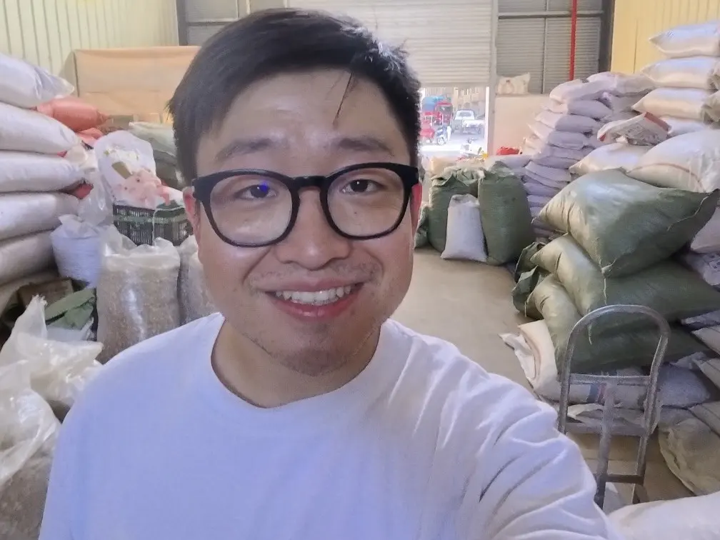 Fu Yang smiling in a warehouse with sacks of spice stacked behind him