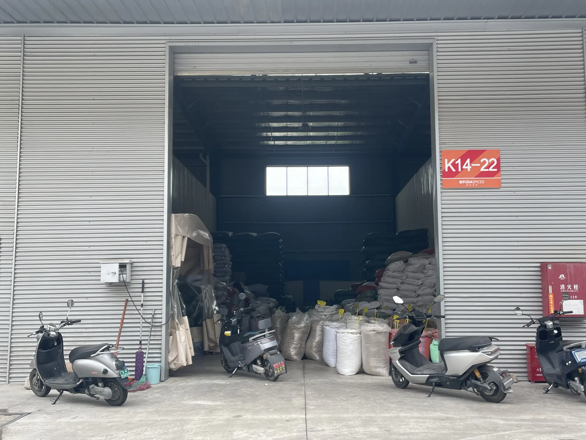 Roller-shutter entrance of the K14-22 warehouse unit, with scooters parked outside and sacks of stock visible inside